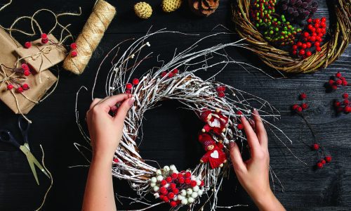 Christmas background. Top view of female hands make a Christmas wreath. Packed gifts and scrolls, spruce branches and tools on wooden table. Workplace for preparing handmade decorations.