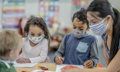 Multi-ethnic group of children colouring at a table while wearing protective face masks to avoid the transfer of germs.